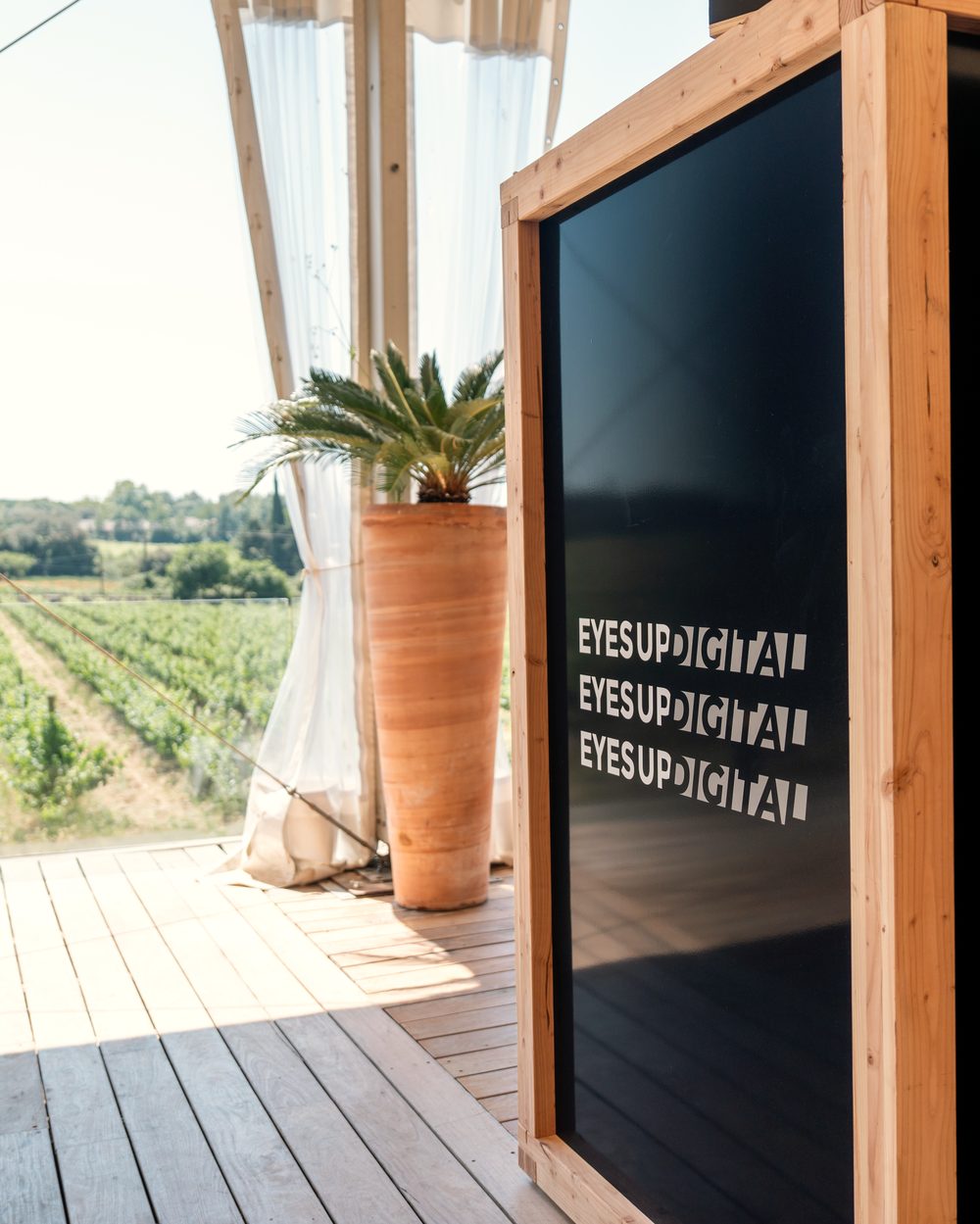 Cube digital en bois sur une terrasse de réception face aux vignes